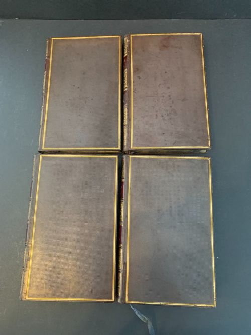 fig 2. A set of four early 19th-century leather-bound books featuring gilt tooling and titles along their dark reddish-brown spines.