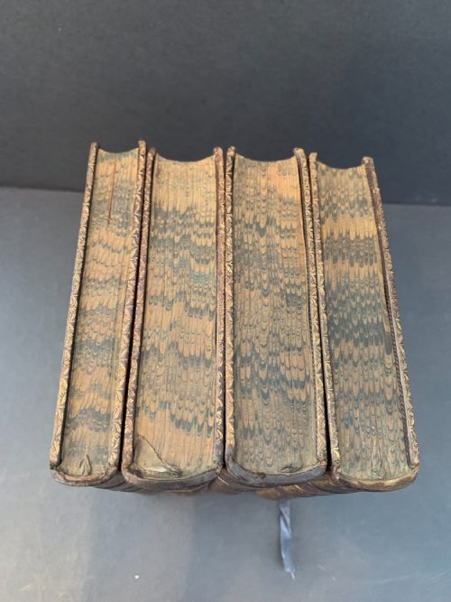 fig 3. A set of four early 19th-century leather-bound books featuring gilt tooling and titles along their dark reddish-brown spines.