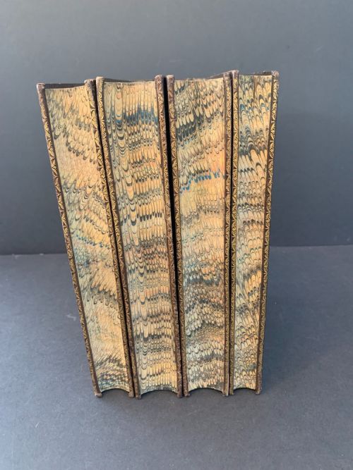 fig 4. A set of four early 19th-century leather-bound books featuring gilt tooling and titles along their dark reddish-brown spines.