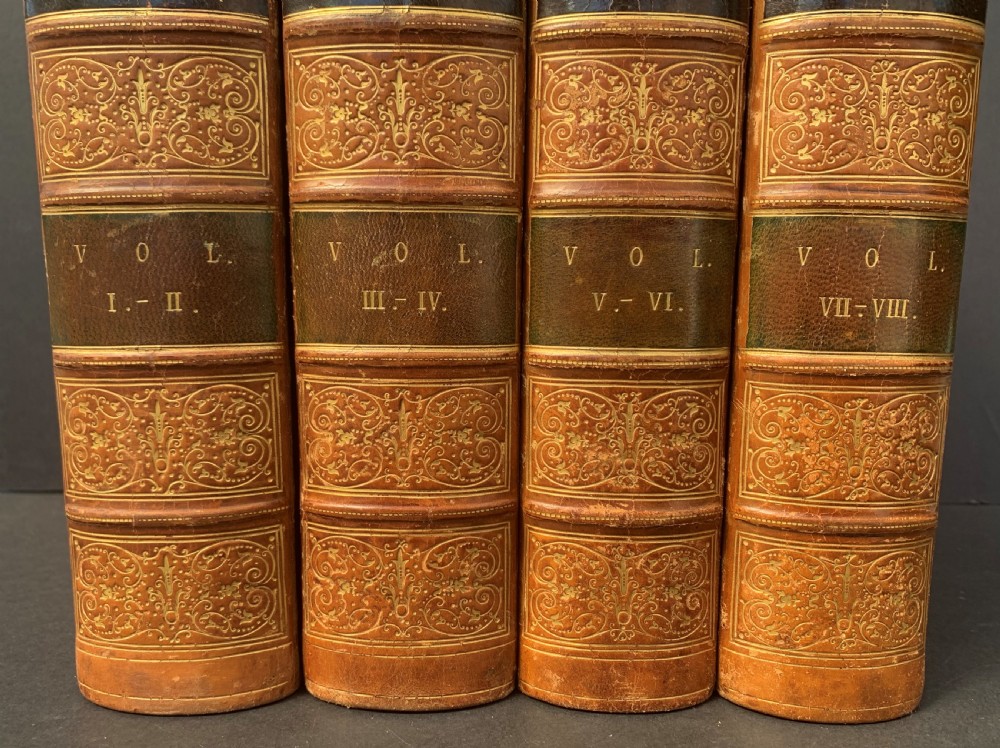 Four antique tan leather-bound volumes with ornate gold gilt decoration and dark title labels on the spines. View VII