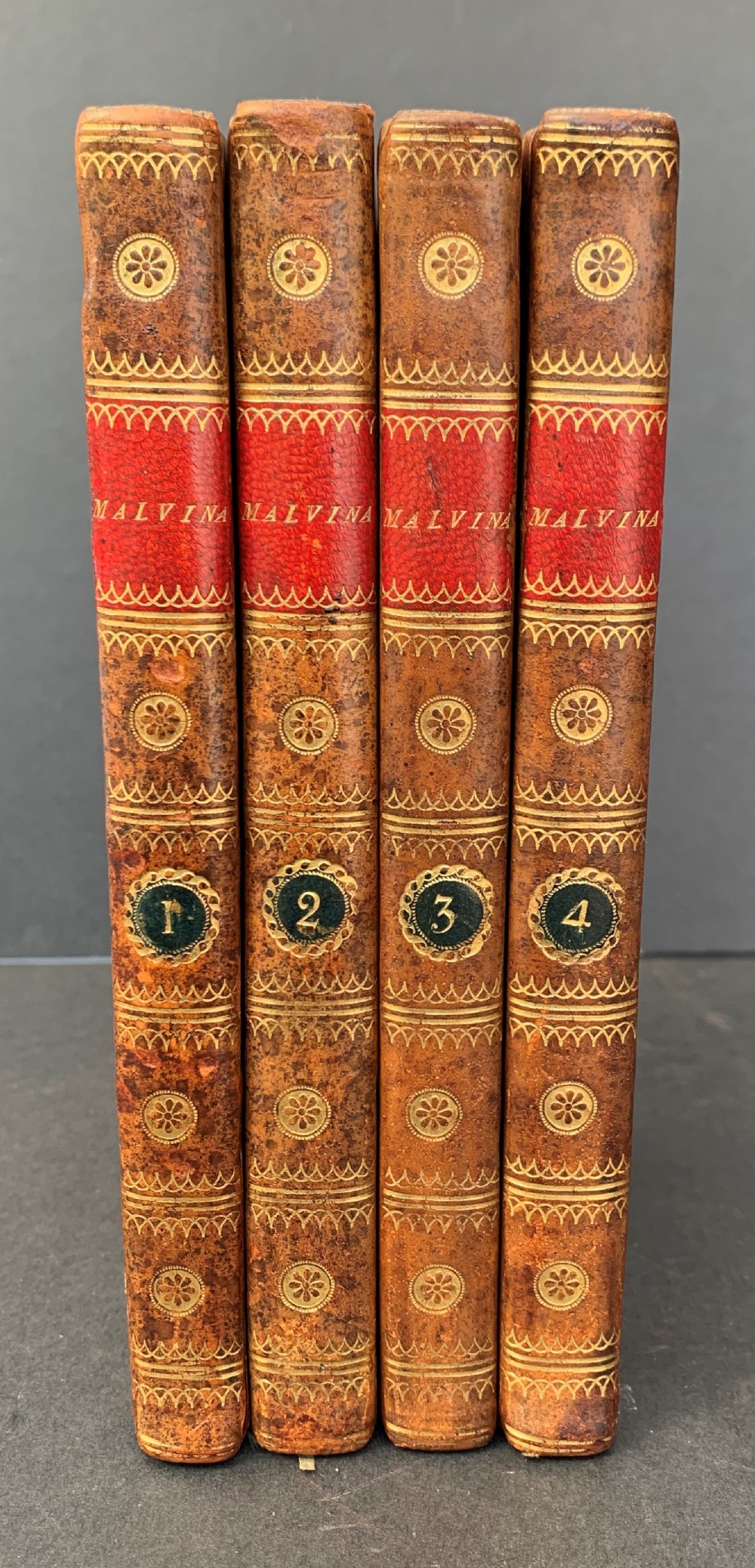 A four-volume set of antique French leather-bound books standing upright, featuring gold gilt tooling and red spine labels numbered one to four.