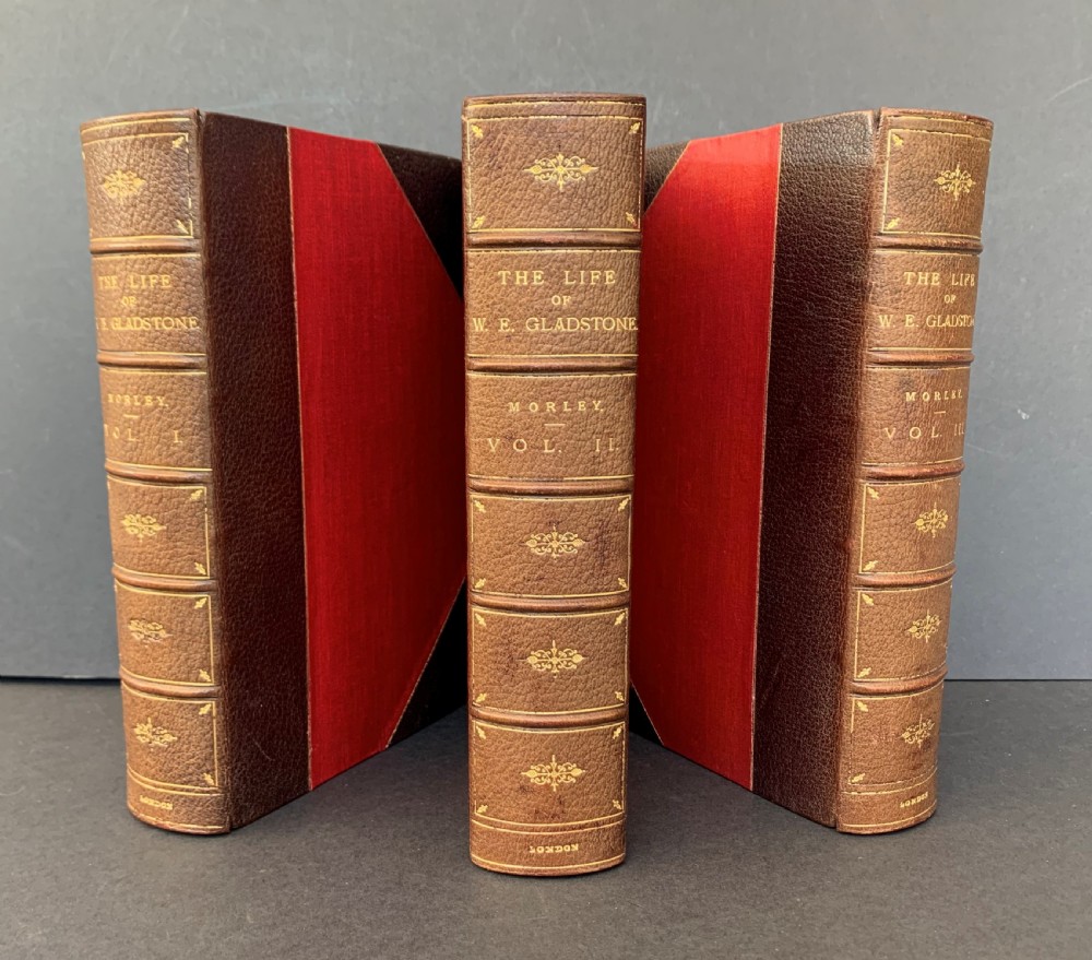 A three-volume set of Edwardian books titled The Life of W E Gladstone, bound in brown half-leather with red cloth sides and gilt spine ornamentation.