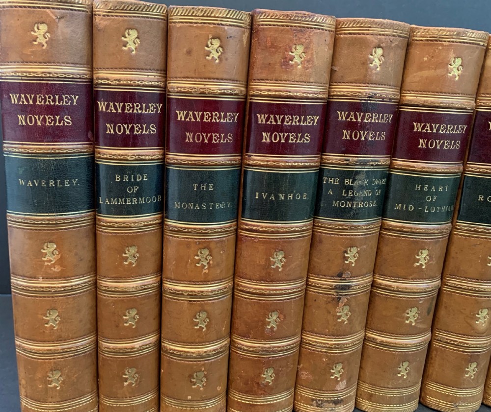 A set of ten Victorian tan leather-bound books titled Waverley Novels displayed side-by-side with gilt tooling and red and green spine labels. View V