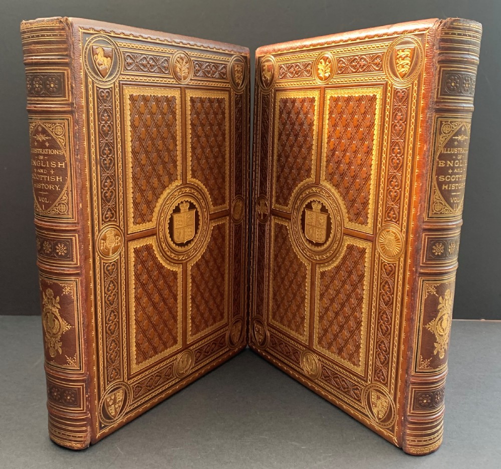 A pair of Victorian leather-bound books featuring gold leaf tooling, crest motifs, and embossed geometric patterns on the brown boards and spines.