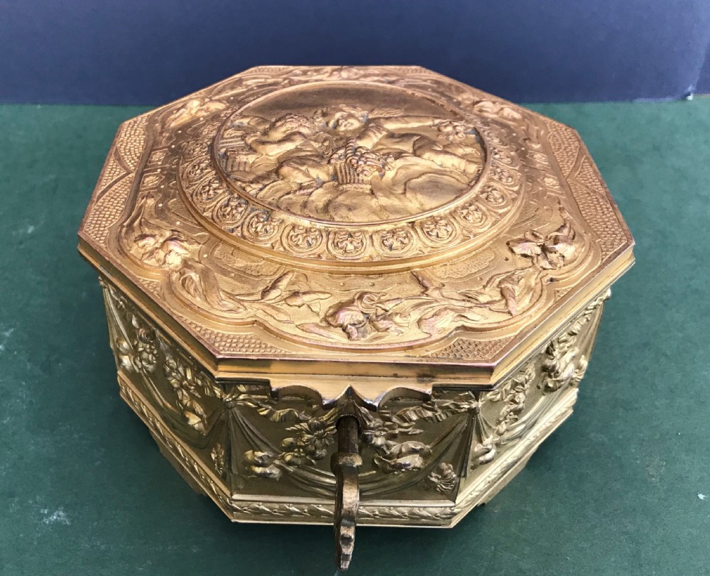 An octagonal French gilded copper jewellery casket decorated with detailed relief carvings of cherubs and floral garlands.