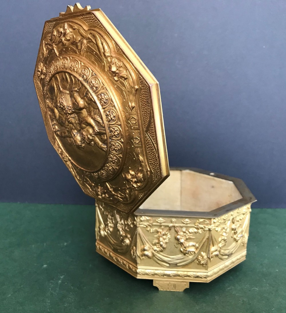 An octagonal French gilded copper jewellery casket decorated with detailed relief carvings of cherubs and floral garlands. View IX