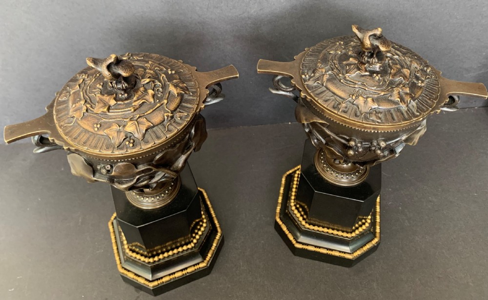 A pair of Victorian cast bronze lidded urns featuring foliage reliefs and bird finials, mounted on octagonal black marble plinths. View II