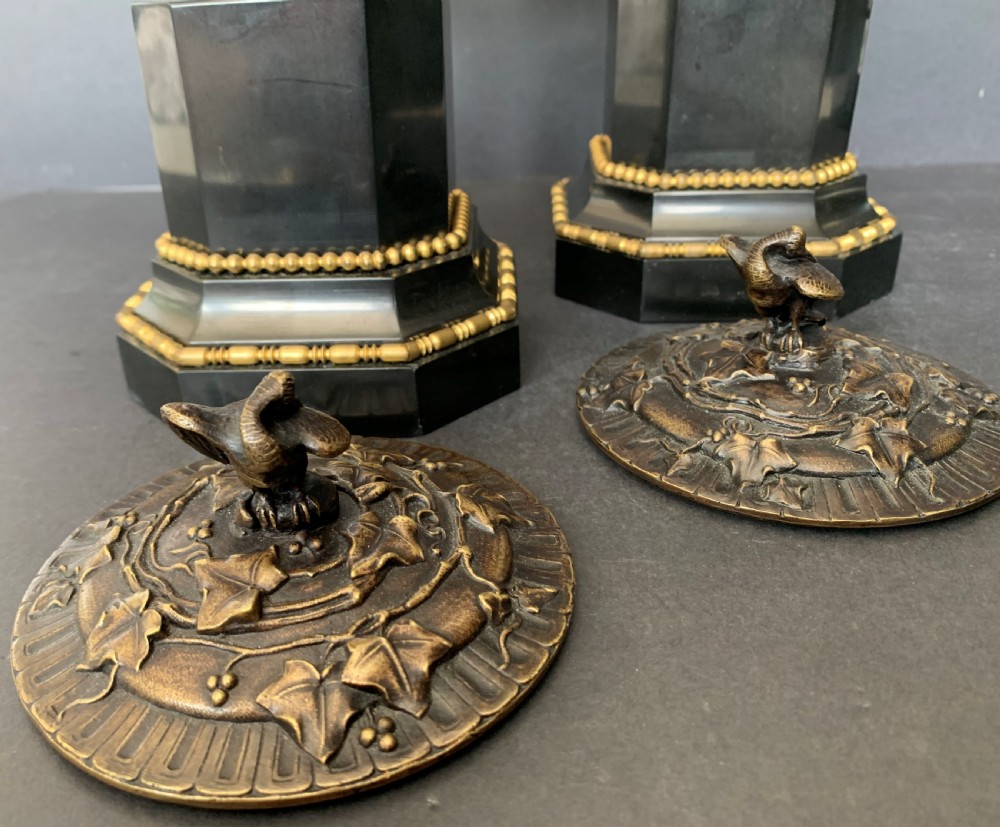A pair of Victorian cast bronze lidded urns featuring foliage reliefs and bird finials, mounted on octagonal black marble plinths. View IV