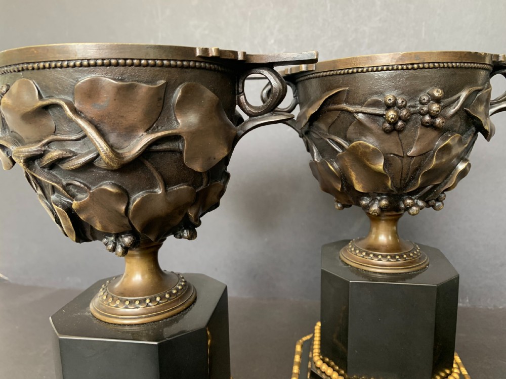 A pair of Victorian cast bronze lidded urns featuring foliage reliefs and bird finials, mounted on octagonal black marble plinths. View V