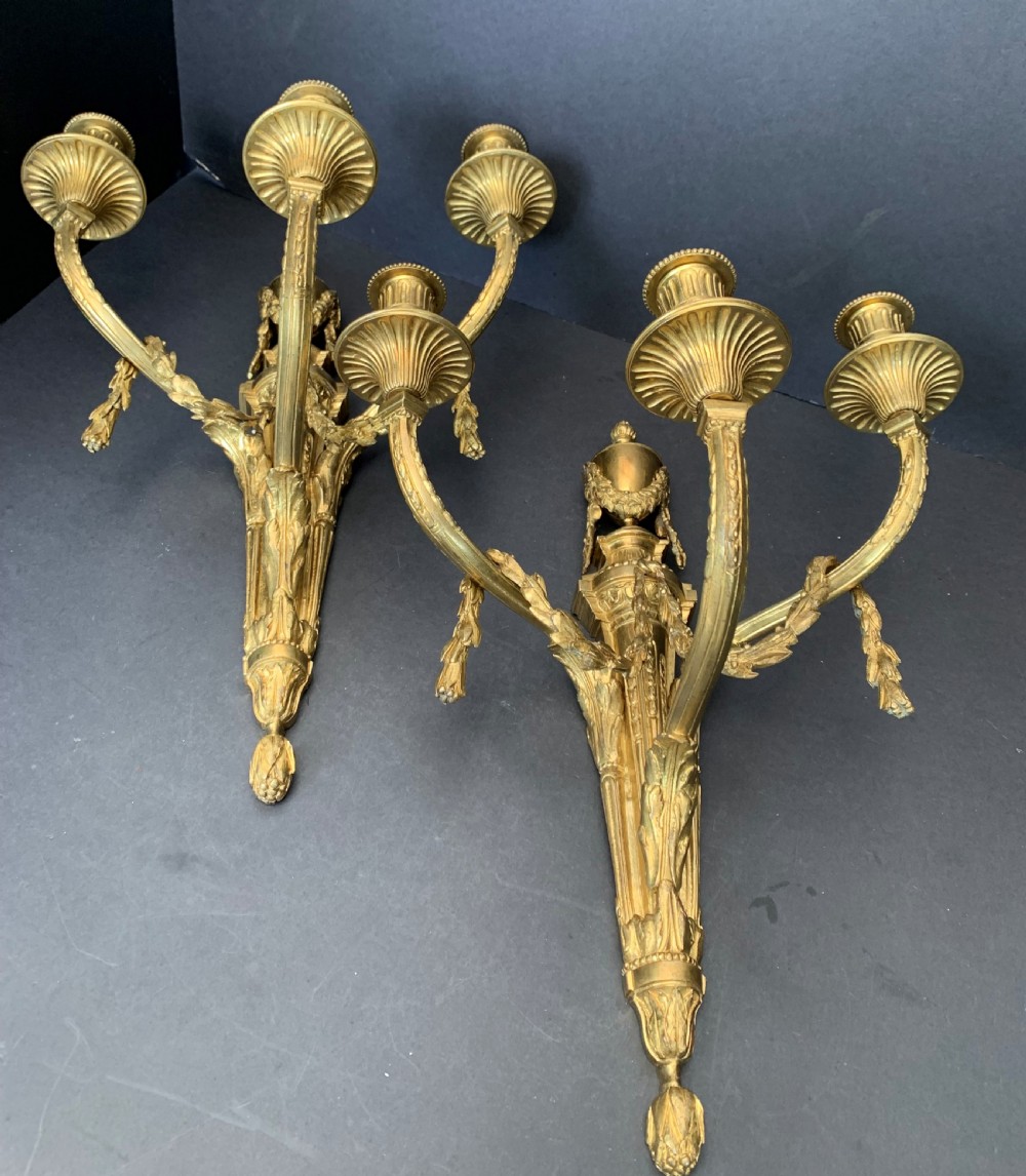 A pair of French gilt bronze wall lights featuring three curving candle branches decorated with leaf swags and topped with urn backplates. View IV