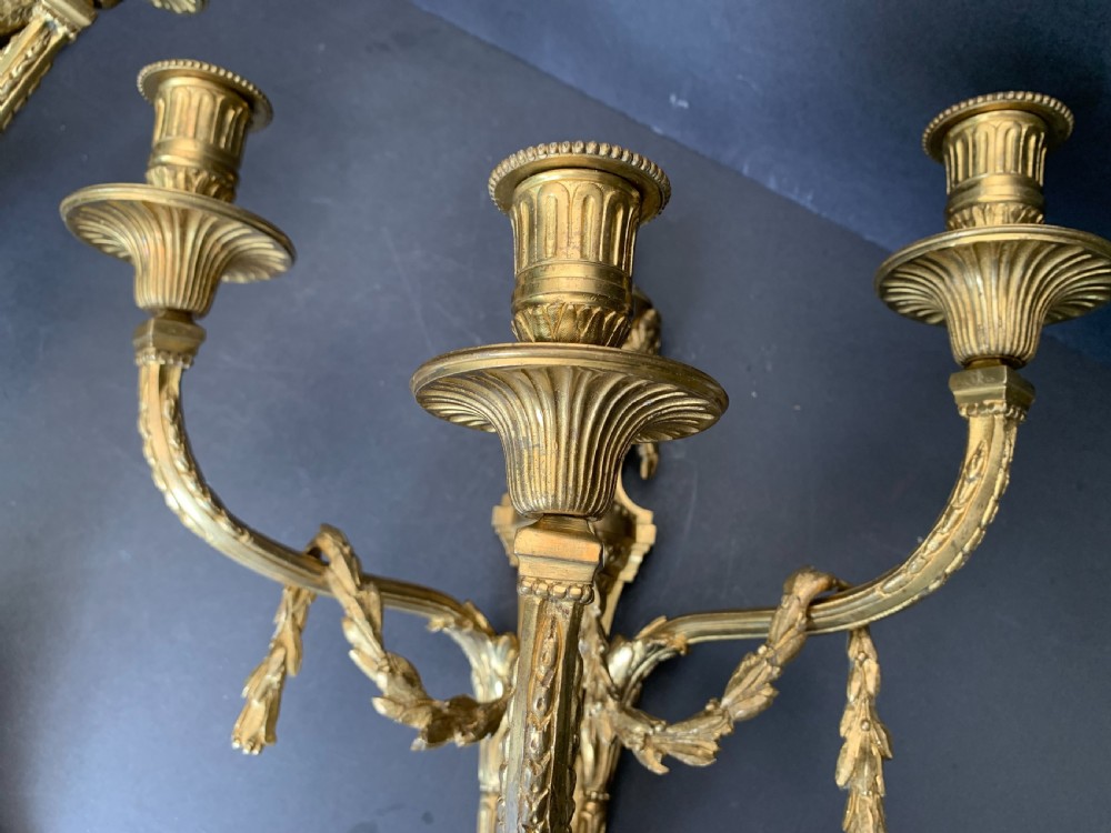 A pair of French gilt bronze wall lights featuring three curving candle branches decorated with leaf swags and topped with urn backplates. View VII