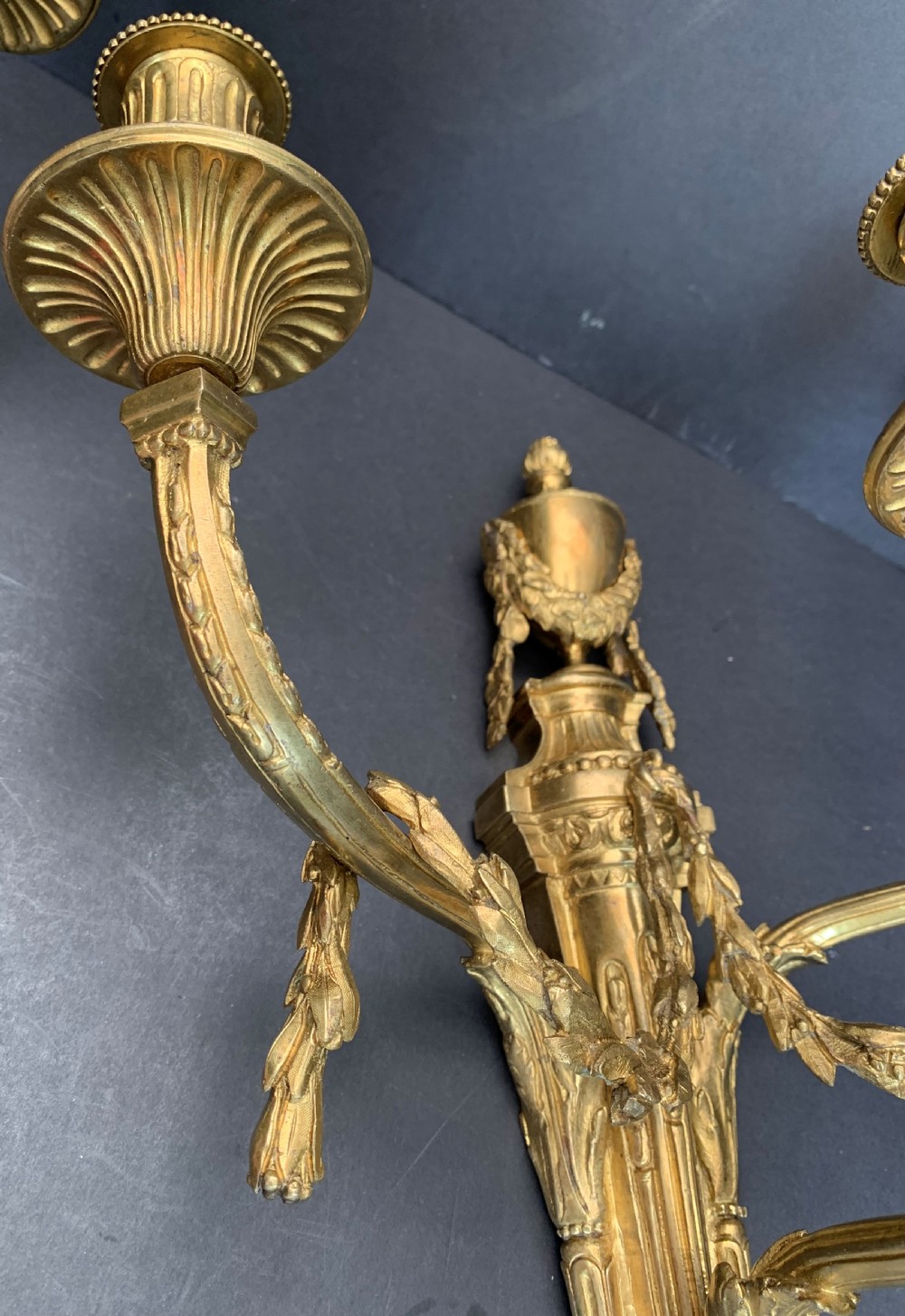 A pair of French gilt bronze wall lights featuring three curving candle branches decorated with leaf swags and topped with urn backplates. View IX
