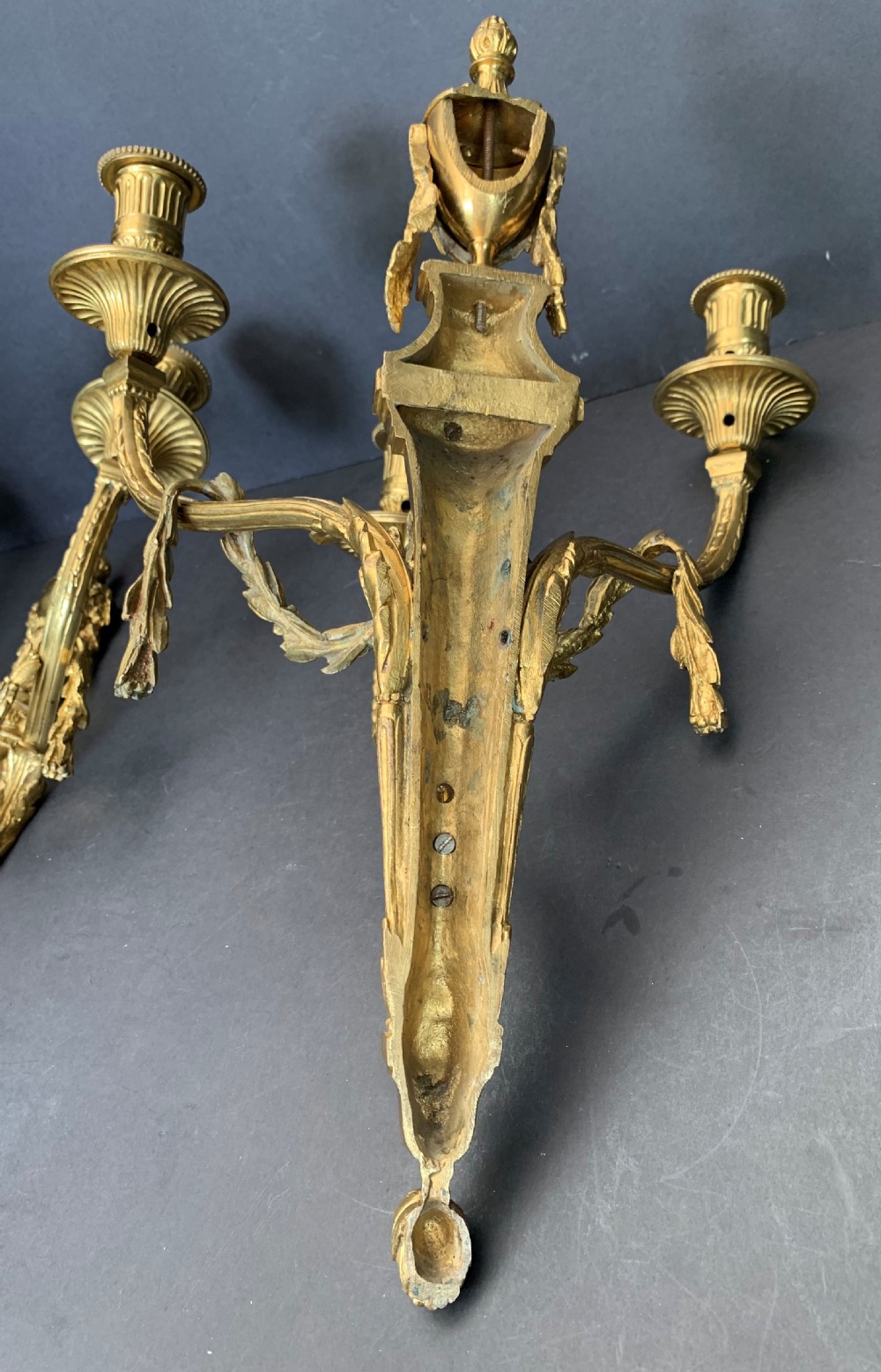 A pair of French gilt bronze wall lights featuring three curving candle branches decorated with leaf swags and topped with urn backplates. View X