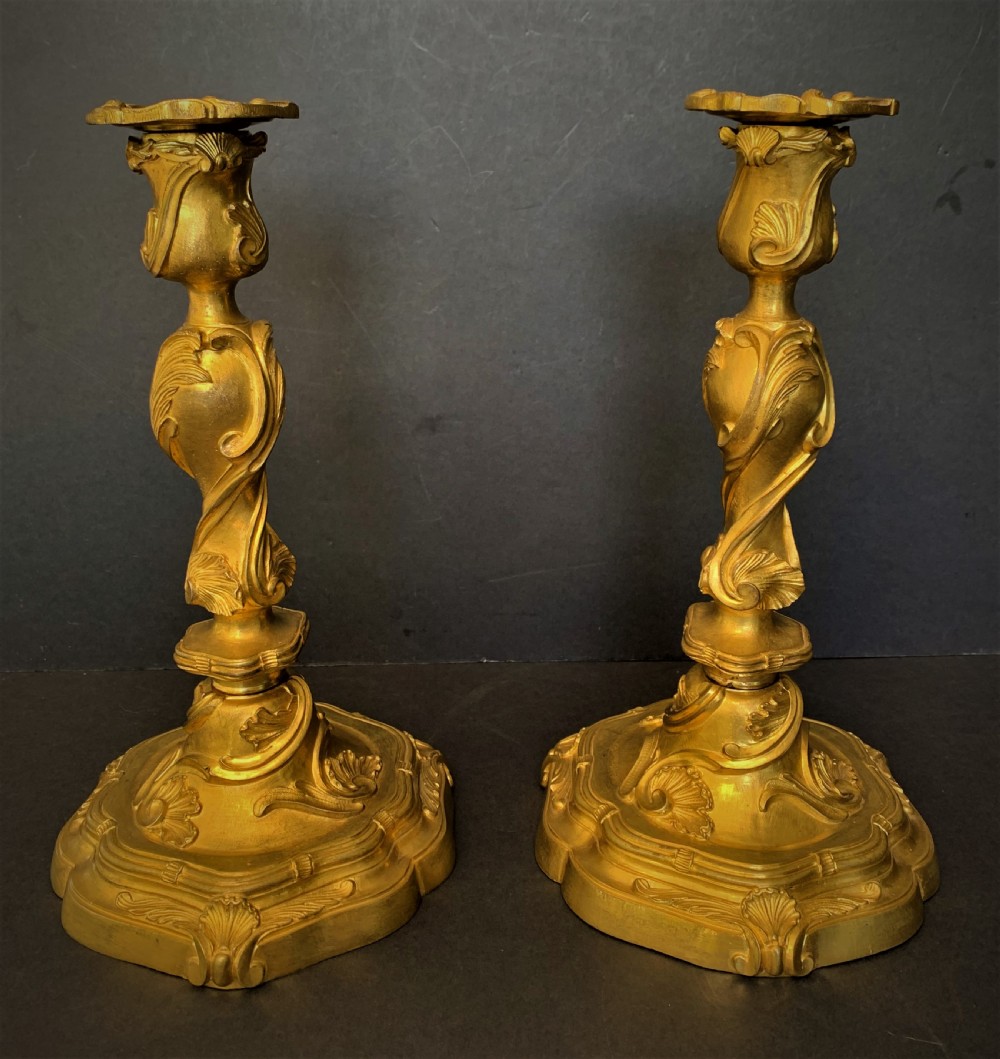 A pair of 19th-century French ormolu candlesticks featuring intricate acanthus leaf carving, rocaille shell motifs, and a gilded finish.