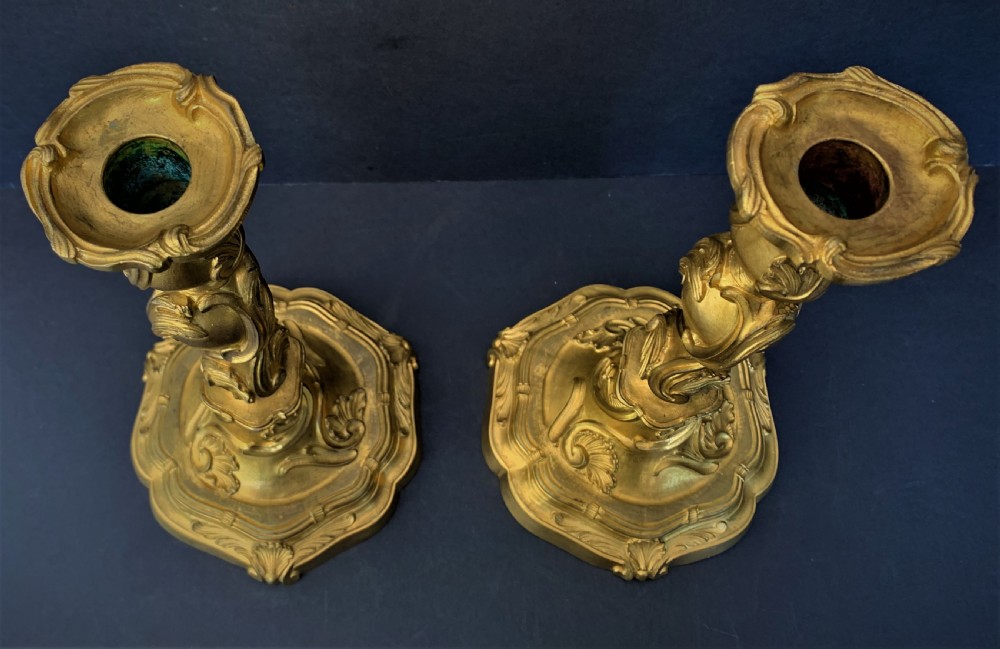 A pair of 19th-century French ormolu candlesticks featuring intricate acanthus leaf carving, rocaille shell motifs, and a gilded finish. View V