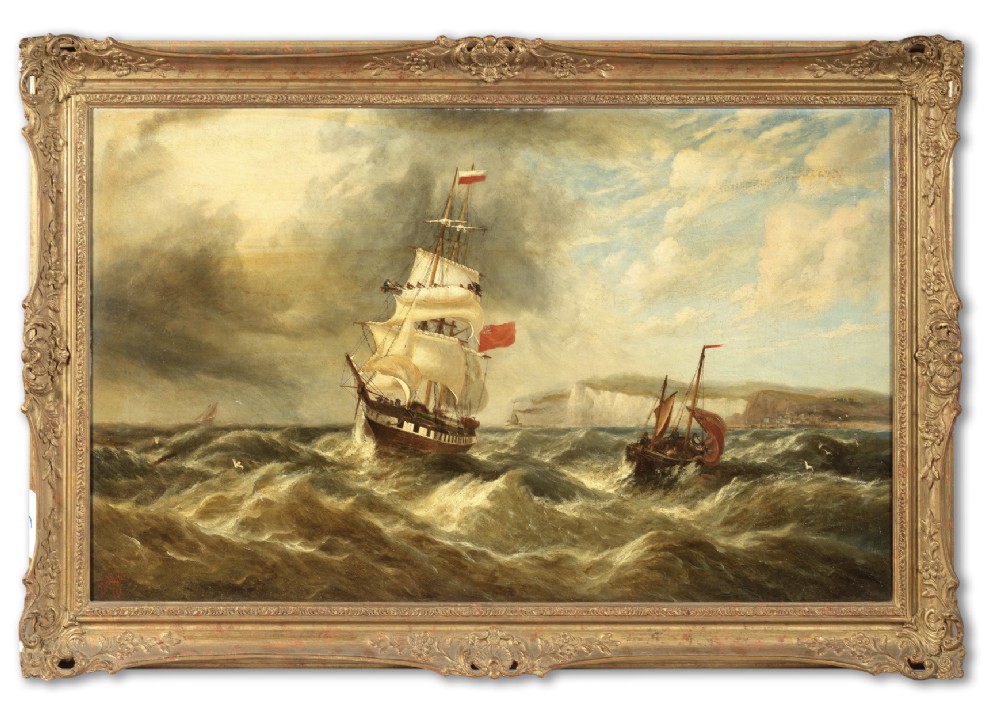 A late nineteenth-century oil painting depicting a British merchant ship in rough seas off a rocky coastline, presented in an ornate gilt frame.