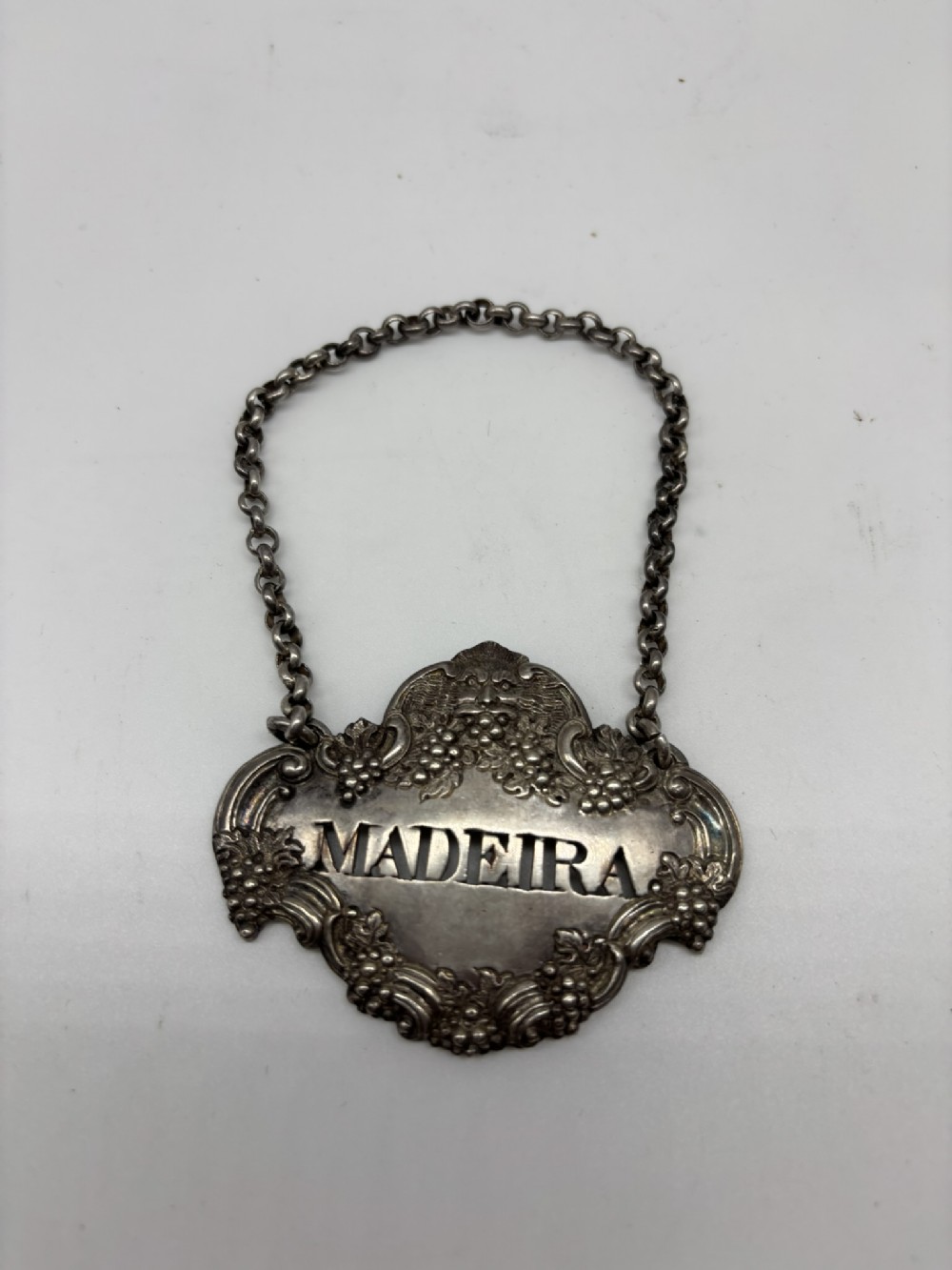 A Georgian silver Madeira decanter label featuring relief grape motifs and pierced lettering suspended from a fine silver chain.