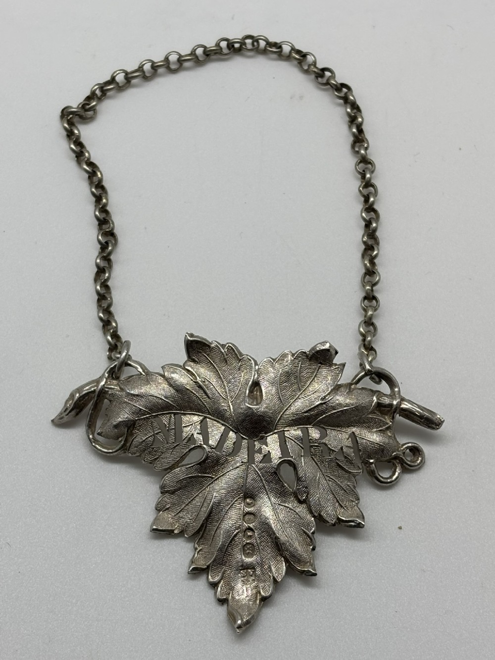 An early Victorian sterling silver wine label in the shape of a vine leaf with the word MADEIRA pierced across the centre, attached to a chain.