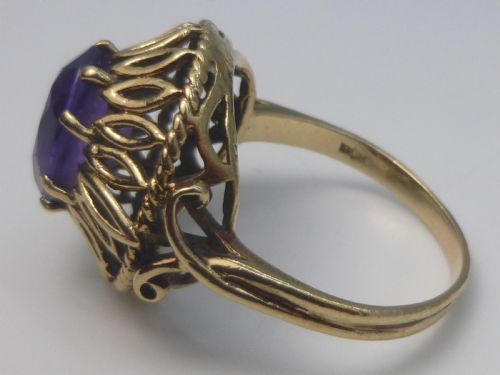 fig 1. A gold dress ring featuring an oval facet-cut purple amethyst gemstone surrounded by a pierced openwork petal border.