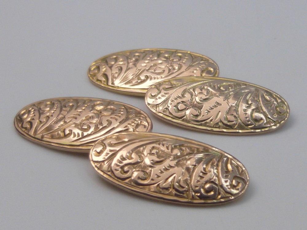 A set of four Edwardian nine-carat rose gold oval cufflink faces with hand-engraved scrollwork motifs.