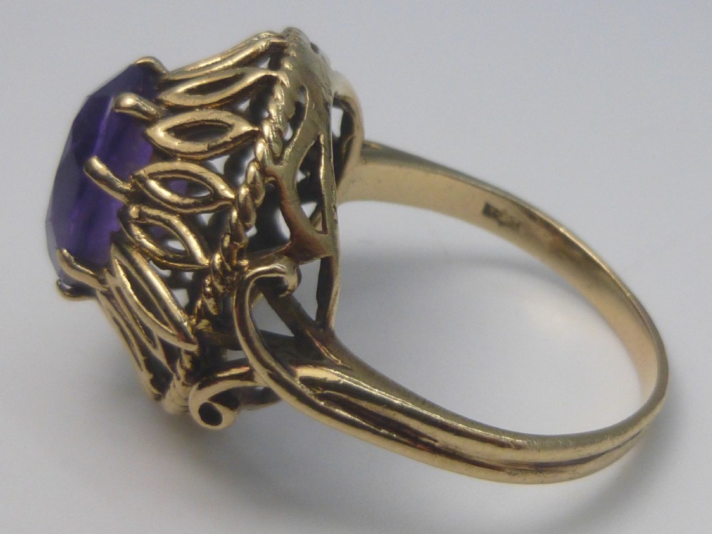 A gold dress ring featuring an oval facet-cut purple amethyst gemstone surrounded by a pierced openwork petal border. View II