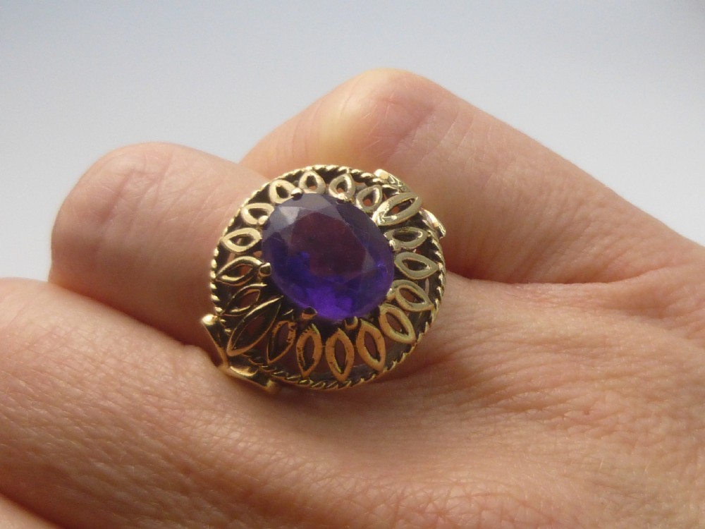 A gold dress ring featuring an oval facet-cut purple amethyst gemstone surrounded by a pierced openwork petal border. View V