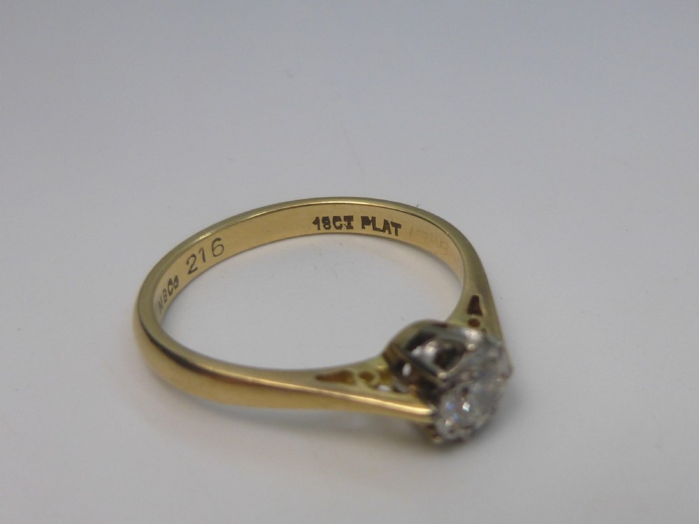 A yellow gold solitaire ring featuring a single round brilliant-cut diamond held in a white metal claw setting. View IV