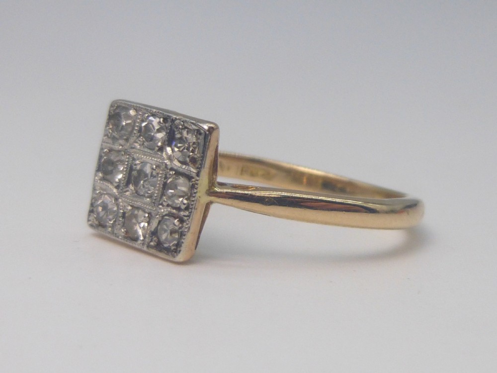 An Edwardian ring featuring a square setting containing nine diamonds in a three-by-three grid atop an 18ct yellow gold band. View V
