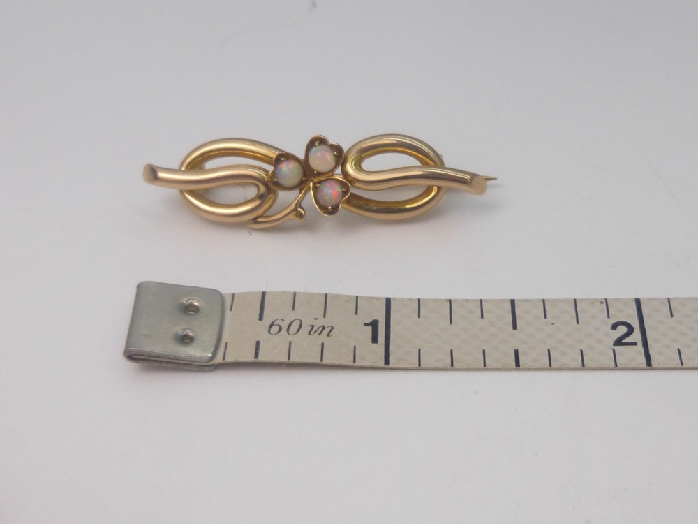 An Edwardian 15ct gold brooch featuring three cabochon opals arranged in a clover setting atop an intertwined gold loop design. View II