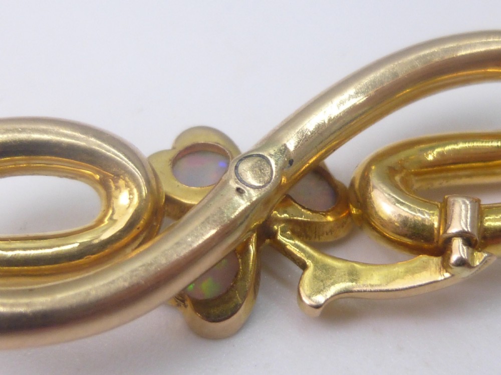 An Edwardian 15ct gold brooch featuring three cabochon opals arranged in a clover setting atop an intertwined gold loop design. View IV