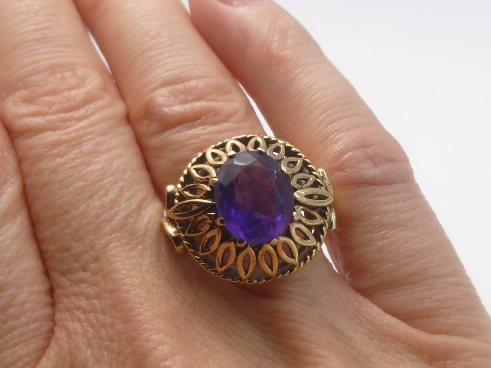 A gold dress ring featuring an oval facet-cut purple amethyst gemstone surrounded by a pierced openwork petal border.