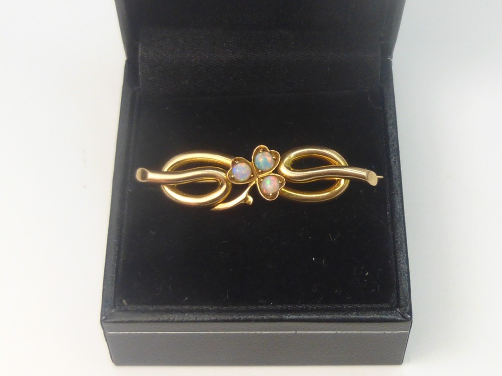 An Edwardian 15ct gold brooch featuring three cabochon opals arranged in a clover setting atop an intertwined gold loop design.