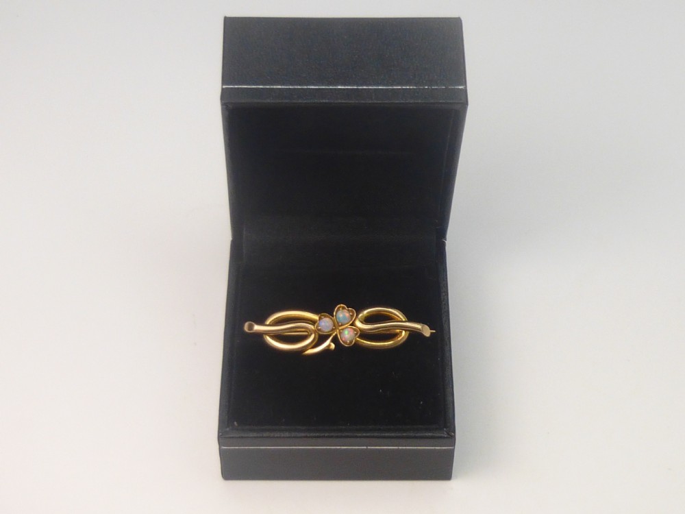 An Edwardian 15ct gold brooch featuring three cabochon opals arranged in a clover setting atop an intertwined gold loop design. View VI