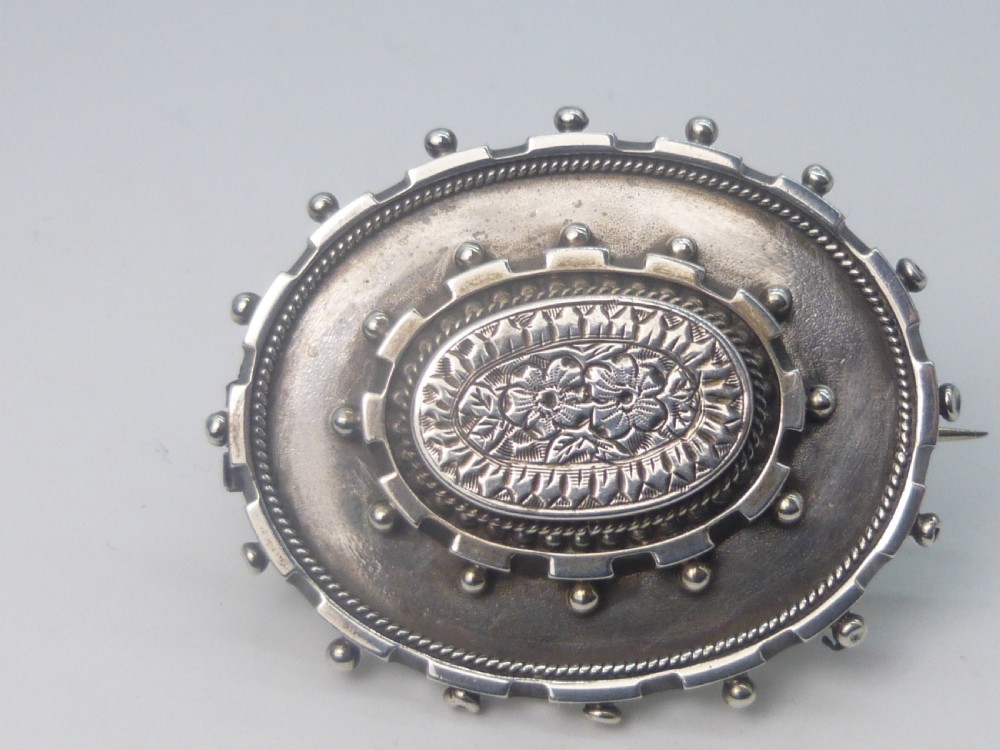 An oval Victorian silver locket brooch featuring an engraved floral centre, rope-twist edging, and a beaded border.