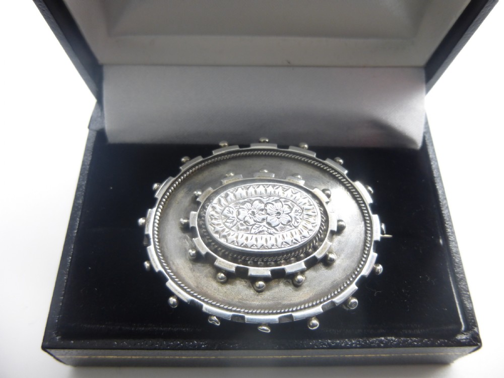 An oval Victorian silver locket brooch featuring an engraved floral centre, rope-twist edging, and a beaded border. View II