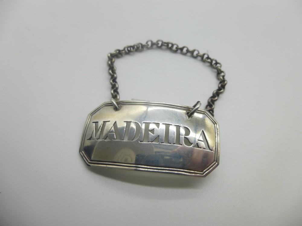 A rectangular William IV sterling silver decanter label with clipped corners engraved with the word Madeira and attached to a silver link chain. View II