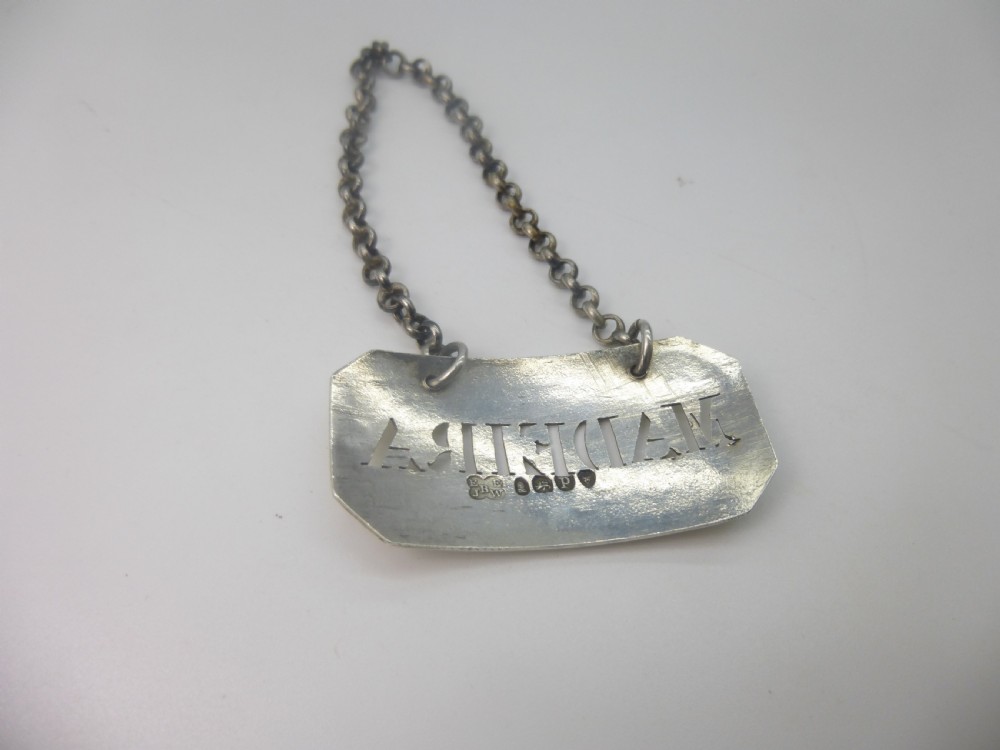 A rectangular William IV sterling silver decanter label with clipped corners engraved with the word Madeira and attached to a silver link chain. View IV