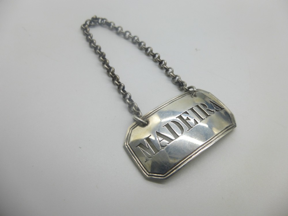 A rectangular William IV sterling silver decanter label with clipped corners engraved with the word Madeira and attached to a silver link chain. View VII