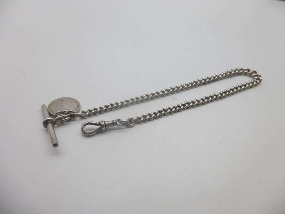 A sterling silver Albert pocket watch chain featuring curb links, a T-bar, a swivel clasp, and an attached silver coin fob against a plain background.