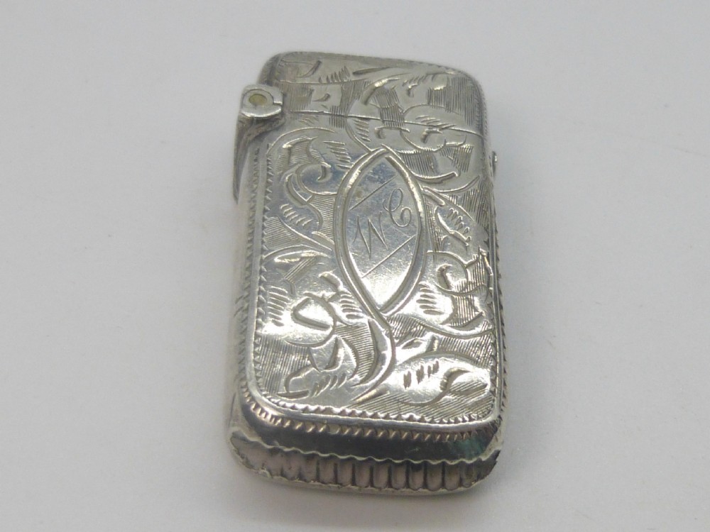 An antique silver vesta case featuring detailed foliate scroll engraving and a central oval monogrammed cartouche.