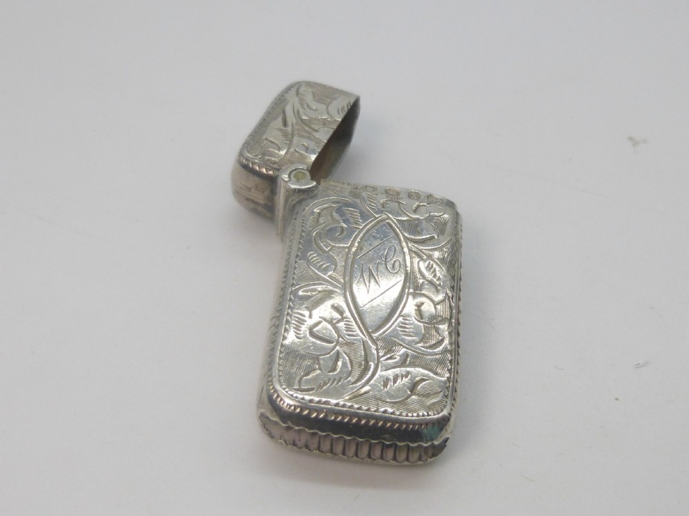 An antique silver vesta case featuring detailed foliate scroll engraving and a central oval monogrammed cartouche. View IV