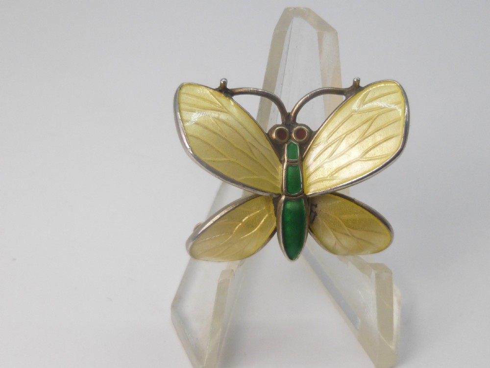 A silver butterfly brooch featuring yellow guilloche enamel wings, a green enamelled body, and red accent eyes.