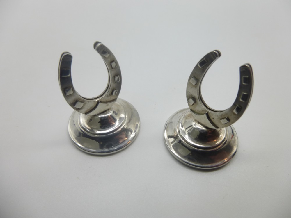 A pair of sterling silver menu card holders featuring horseshoe-shaped tops mounted on circular stepped bases.