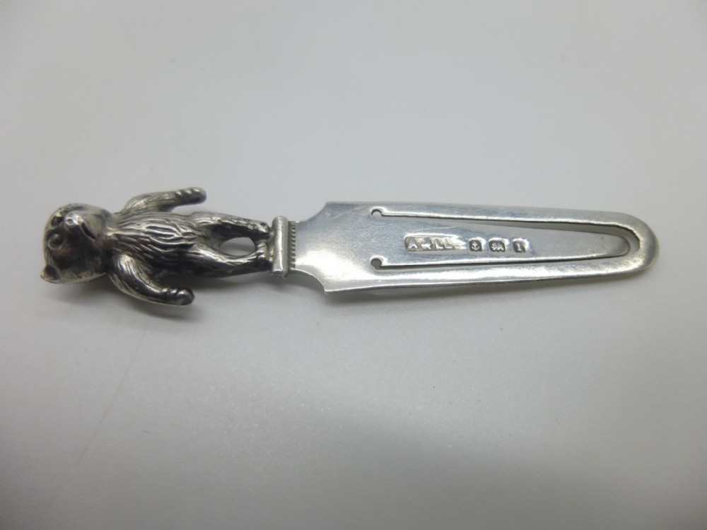 An antique sterling silver bookmark featuring a cast teddy bear finial at the top and struck hallmarking stamps along the flat page clip section.