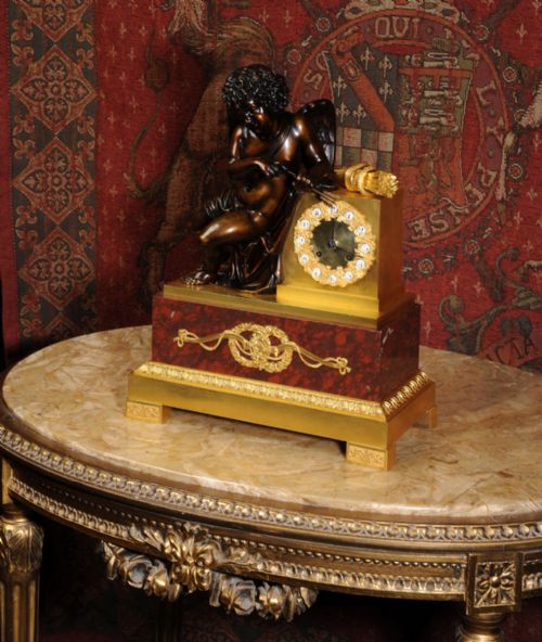 fig 2. A French Empire style dark bronze and gilt ormolu mantel clock featuring a seated Cupid beside the clock dial, supported on a red marble base.