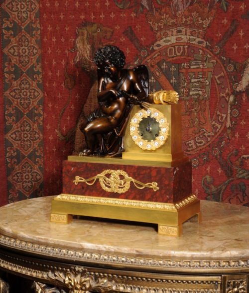fig 3. A French Empire style dark bronze and gilt ormolu mantel clock featuring a seated Cupid beside the clock dial, supported on a red marble base.