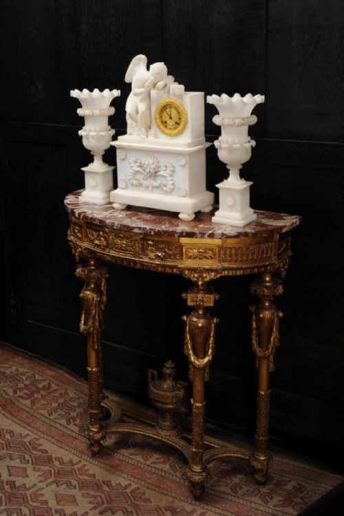 fig 4. A three-piece white alabaster clock set featuring a central timepiece surmounted by a sculpted Cupid figure after Falconet, flanked by two matching carved urns.