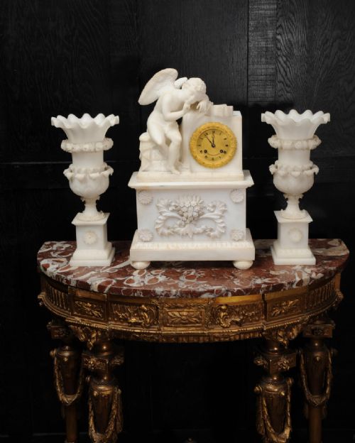 fig 5. A three-piece white alabaster clock set featuring a central timepiece surmounted by a sculpted Cupid figure after Falconet, flanked by two matching carved urns.
