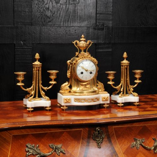 fig 1. A French Louis XVI style clock garniture set featuring a central gilt bronze and white marble mantel clock flanked by two matching two-light candelabra.