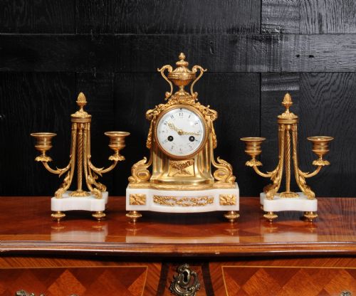 fig 2. A French Louis XVI style clock garniture set featuring a central gilt bronze and white marble mantel clock flanked by two matching two-light candelabra.